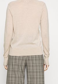 Pull beige à manches longues avec un col et des poignets côtelés, présentant une texture douce. Associé à un pantalon large en laine à carreaux.