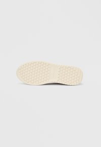 Εκρού σόλα παπουτσιού με κυκλικά σχέδια λαβής και ορθογώνιο τμήμα στο κέντρο σε ανοιχτό γκρι φόντο.