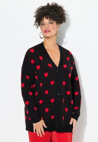 Schwarze Strickjacke mit rotem Herzmuster, Knopfverschluss vorne und gerippten Bündchen. Das strukturierte Strickmaterial verleiht ein kuscheliges Aussehen.