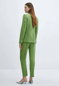 Groene op maat gemaakte pak met een gestructureerde blazer en slim fit broek, gemaakt van een textuurstof. Voorzien van knoopaccenten op de blazer.