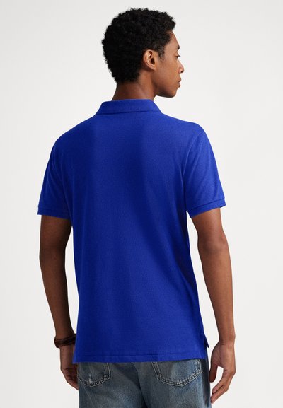 Camisa polo azul com textura suave, mangas curtas e gola. Apresenta aberturas laterais na bainha para maior conforto.