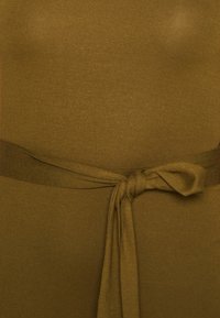 Olivově zelené šaty s přiléhavým korzátem a širokým, zavázaným páskem v oblasti pasu. Vyrobené z hladké, pružné pleteniny.