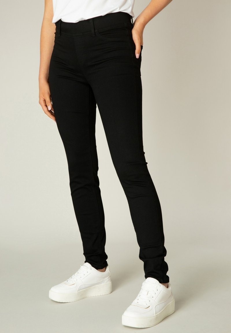 Zwarte stretch jeans met een slim fit, voorzien van een hoge tailleband en subtiele stikdetails. Gecombineerd met witte platform sneakers.