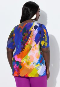 Kleurrijk kortermig shirt met een abstract ontwerp van verfspatten in blauw, oranje, roze en geel, gecombineerd met paarse broek.