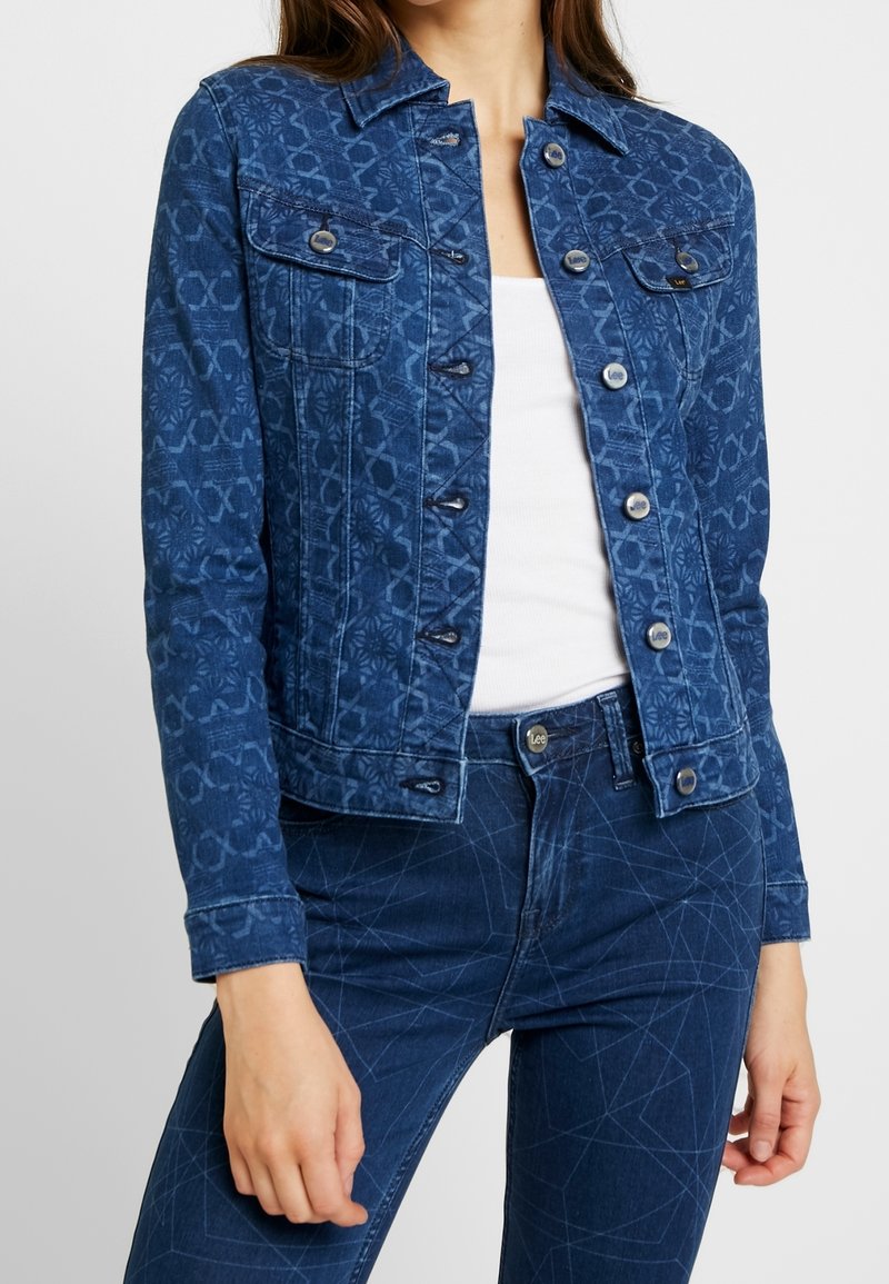 Denim jacket in dark blue with subtle pattern, featuring two chest pockets and silver buttons, paired with matching dark blue jeans.