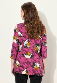 Túnica morada con patrón floral en blanco y naranja, mangas de 3/4, corte holgado, con dobladillo curvado y tela texturizada.
