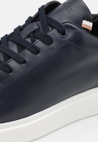 Baskets en cuir bleu marine avec semelle en caoutchouc blanche contrastante, bout rond, design à lacets plats et logo subtil près du talon.