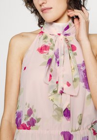 Bloemenjurk van lichtgewicht, doorschijnende stof, met een pastelroze basis en paarse en rode bloemen, een halterhals en een strikdetail.