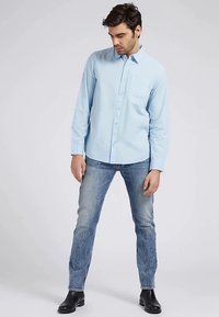 Hellblaues Hemd mit langen Ärmeln, Knopfleiste und Brusttasche, kombiniert mit ausgewaschenen blauen Jeans und schwarzen Stiefeletten. Glatte Stoffstruktur.