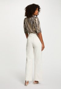 Blouse courte à manches courtes avec un motif métallique et un col haut, associée à un pantalon large taille haute blanc et des talons blancs à lanières.