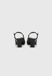 Black heeled sandals with a block heel, adjustable ankle strap, and embellished detailing on the back. Smooth texture and sleek design.