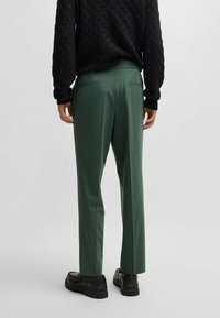 Pantalons ajustés verts avec une texture lisse, dotés de poches arrière et d'un design à jambes droites. Associés à un pull noir à motifs.