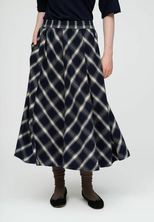 Femme portant une jupe midi trapèze à carreaux bleu marine et blanc avec taille élastique, associée à des chaussettes côtelées marron et des ballerines noires.