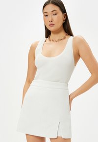 Hvid ribbet tanktop med brede stropper, sat sammen med en tekstureret hvid miniskirt med en enkelt frontslids og en tætsiddende talje.
