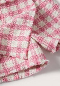 Roze-wit geruit stof met een geweven textuur, met rafelige randen en een zachte uitstraling. Geschikt voor diverse textieltoepassingen.