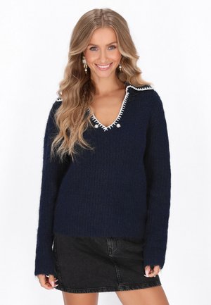 Maglione in maglia blu navy con scollatura a V e rifiniture bianche. Presenta maniche lunghe e bottoni decorativi vicino alla scollatura. Texture morbida.