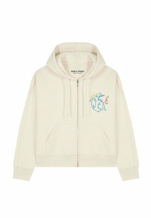 Sweat à capuche crème zippé avec un requin bleu brodé sur la poitrine, tenant une fleur rose avec des feuilles vertes et des rayons de soleil jaunes derrière.
