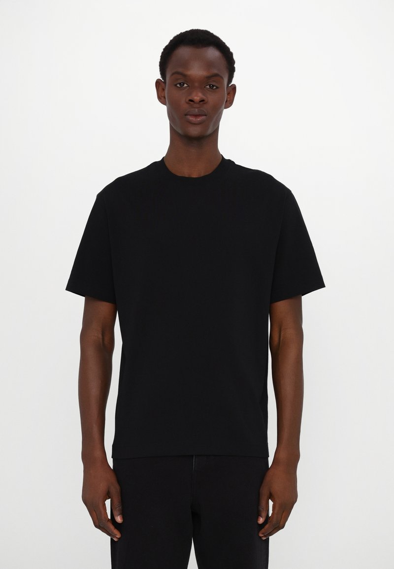 Tricou din bumbac negru, cu guler clasic rotund și mâneci scurte, având o croială relaxată și o textură netedă.