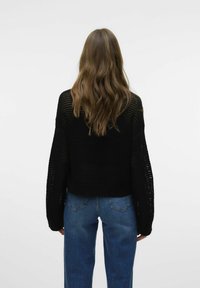 Zwart cropped trui met een losse brei-ontwerp en lange mouwen. Gecombineerd met hoge taille blauwe jeans, voor een casual look.