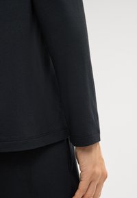 Czarny top z długim rękawem, okrągłym dekoltem i prostym dołem. Miękka tkanina, widoczne przeszycia i luźny krój. Element dopasowanego zestawu.