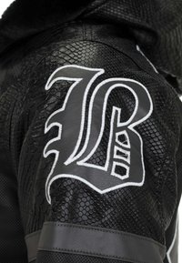 Black leather jacket featuring textured snake skin pattern, embroidered lettering, and contrasting accents in grey. Detailed stitching visible.