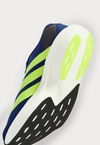 Tengerészeti sportcipő neon zöld csíkokkal, gumitalppal, amely körkörös bordázattal rendelkezik, és párnázott fehér középtalppal.