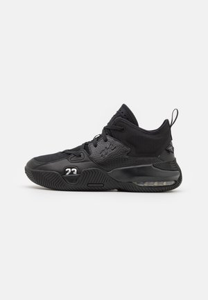 Black athletic shoe with mesh and leather upper, textured accents, cushioned sole, and visible air unit in the heel. Features a prominent logo.