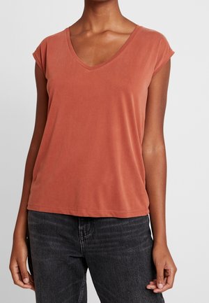 Top z krótkim rękawem i dekoltem w serek w kolorze terakoty, gładka faktura, luźny krój, kontrastowe przeszycia, w połączeniu z ciemnymi dżinsami.