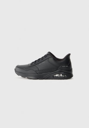Black athletic shoes with a smooth synthetic upper, lace-up design, round toe, and visible air cushioning in the sole. Textured accents included.