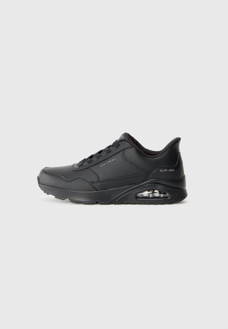 Chaussures de sport noires avec une tige synthétique lisse, un design à lacets, un bout rond et un amorti d'air visible dans la semelle. Des accents texturés sont inclus.