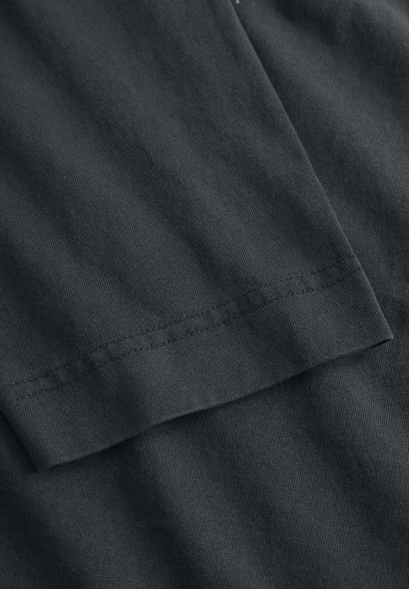 Tissu gris foncé avec une texture côtelée, mettant en valeur un gros plan de la manche et de l'ourlet avec des détails de couture visibles.