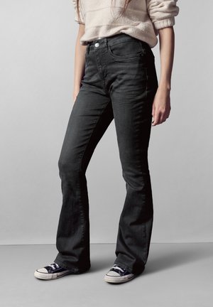 Vaqueros acampanados negros para mujer, fabricados en denim de textura suave, con una cintura alta, diseño de cinco bolsillos y cierre de botón.