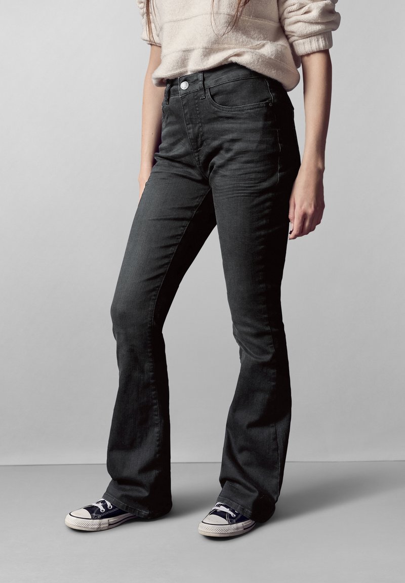 Vaqueros acampanados negros para mujer, fabricados en denim de textura suave, con una cintura alta, diseño de cinco bolsillos y cierre de botón.