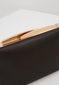Pochette rectangulaire noire en tissu lisse avec une fermeture à clip métallique doré brillant sur une surface blanche.