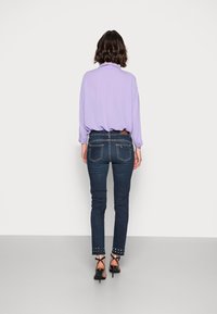 Ljuslila långärmad skjorta kombinerad med mörkblå skinny jeans med nitar vid fållen och bakfickorna.