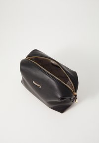 Borsa cosmetica in pelle nera textured con zip dorata, caratterizzata da un logo sulla parte anteriore e una fodera stampata all'interno. Forma arrotondata.