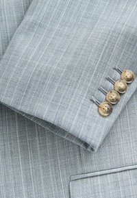 Manche d'un costume ajusté gris clair avec de subtiles rayures verticales, comportant quatre boutons ronds couleur marron clair et des coutures contrastées.