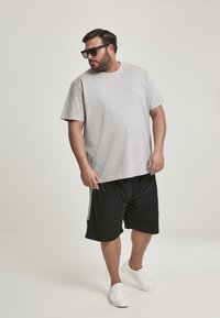 T-shirt en coton gris à manches courtes, associé à un short de sport noir avec des rayures blanches sur les côtés, porté avec des baskets blanches.