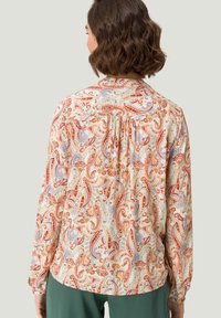 Blusa de manga larga en una tela ligera con un patrón de paisley en rojo, azul y crema, con detalles fruncidos en la parte posterior.