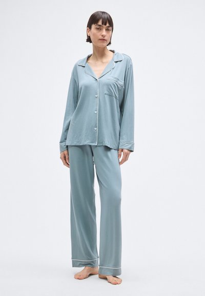 Világoskék pizsamaszett puha anyagból, hosszú ujjakkal, gombos elejű zsebbel, valamint kontrasztos szegélyezéssel az ujjak és a gallér mentén.