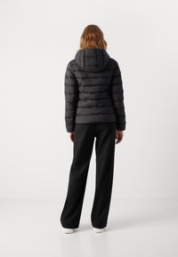 Puffer jacket in black with horizontal stitching, hood, and zip closure; paired with loose black pants and white-soled shoes.