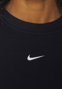 Czarna bawełniana koszulka z okrągłym dekoltem i małym białym logo Nike na piersi. Materiał ma gładką teksturę i dopasowany krój.
