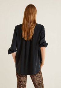 Maglietta nera a maniche lunghe con polsini arrotolati, texture liscia, vestibilità rilassata e orlo dritto, abbinata a pantaloni con stampa leopardata.