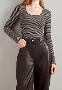 Černobílé pruhované tričko s dlouhým rukávem a kulatým výstřihem, doplněné o černé hladké kožené kalhoty s vysokým pasem a přední kapsou.