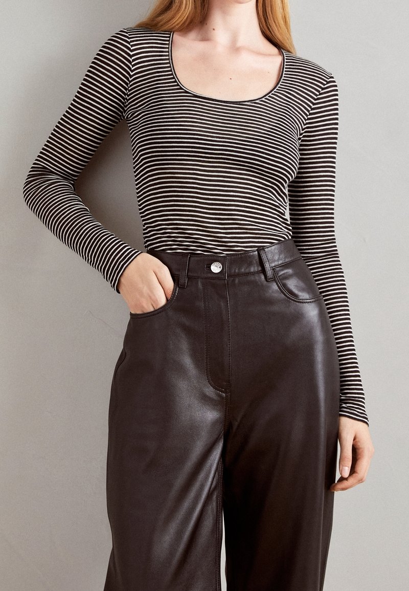 Černobílé pruhované tričko s dlouhým rukávem a kulatým výstřihem, doplněné o černé hladké kožené kalhoty s vysokým pasem a přední kapsou.