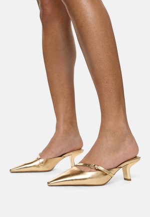 Gold metallic mules with pointed toe, mid-height heel, and a single strap across the instep. Smooth texture with shiny finish.