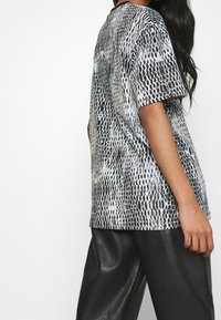 Koszulka z krótkim rękawem w czarno-białym wzorze w węża. Posiada luźny krój, okrągły dekolt oraz gładki, miękki materiał.