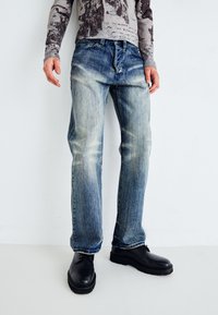Faded blue jeans with a straight fit and light distressing, paired with black chunky shoes. Fabric shows signs of wear and whiskering.