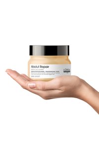 L'Oréal Professionnel Absolut Repair mask in a transparent glass jar, light yellow product inside, with a black lid. Hand holding the jar.