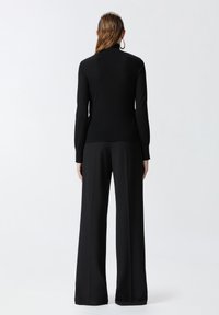 Pull noir à côtes avec un col montant et des manches longues, associé à un pantalon noir à jambes larges. Texture lisse et design ajusté.